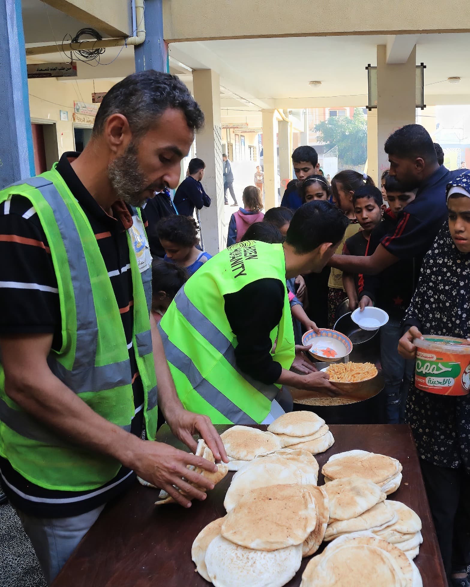 Hidden Humanity volunteers in hi-vis vests distributing fresh bread and hot meals to families at a community kitchen